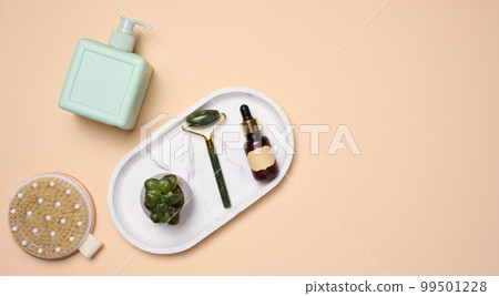 A brown bottle with a paper label and dropper, a massage brush on a beige background, viewed from above. Cosmetic packaging A brown bottle with a paper label and dropper, a massage brush on a beige background, viewed from above. Cosmetic packaging 99501228