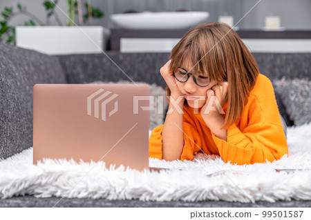 disappointed kid looking at laptop at home on sofa 99501587