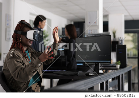 African american system engineer wearing virtual reality goggles working to develop security program in it big data office, software developer with vr headset coding html script with database. African american system engineer wearing virtual reality goggles working to develop security program in it big data office, software developer with vr headset coding html script with database. 99502812