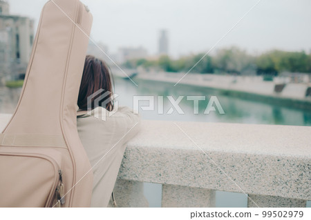 Photo of a woman holding a guitar standing by a bridge Photo of a woman holding a guitar standing by a bridge 99502979