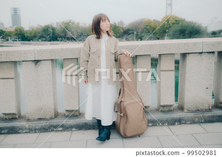 Photo of a woman holding a guitar standing by a bridge Photo of a woman holding a guitar standing by a bridge 99502981