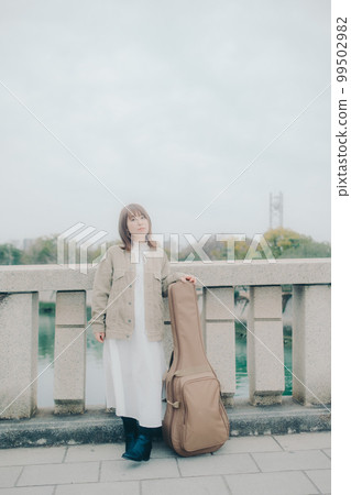 Photo of a woman holding a guitar standing by a bridge Photo of a woman holding a guitar standing by a bridge 99502982