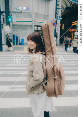 一個女人拿著吉他走在街上的照片 99503061