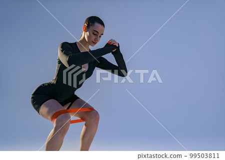 Attractive woman wearing sportswear trains legs with fitness elastic band on studio background 99503811