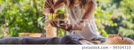 BANNER, LONG FORMAT Nepal Buddha copper singing bowl at spa salon. Young beautiful woman doing massage therapy singing bowls in the Spa against a waterfall. Sound therapy, recreation, meditation 99504310