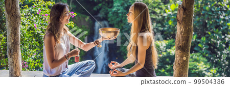 BANNER, LONG FORMAT Nepal Buddha copper singing bowl at spa salon. Young beautiful woman doing massage therapy singing bowls in the Spa against a waterfall. Sound therapy, recreation, meditation 99504386