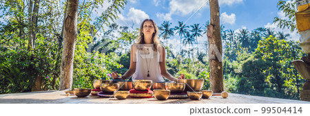 Woman playing on Tibetan singing bowl while sitting on yoga mat against a waterfall. Vintage tonned. Beautiful girl with mala beads meditating BANNER, LONG FORMAT Woman playing on Tibetan singing bowl while sitting on yoga mat against a waterfall. Vintage tonned. Beautiful girl with mala beads meditating BANNER, LONG FORMAT 99504414