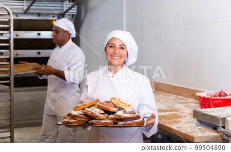 Cheerful woman baker with tray of sweet ensaimadas 99504890
