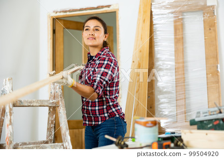 Woman doing home renovation - preparing the door for installation in doorway 99504920