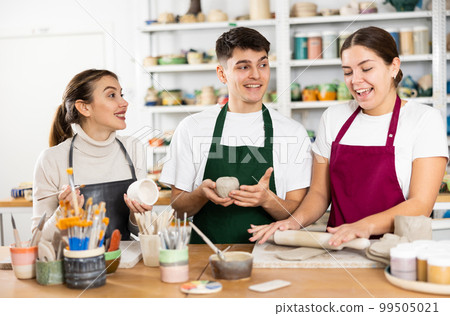 Joyous young man and women sculpting handmade cups 99505021
