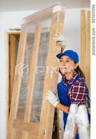 Woman worker carrying wooden door during renovation works 99505099