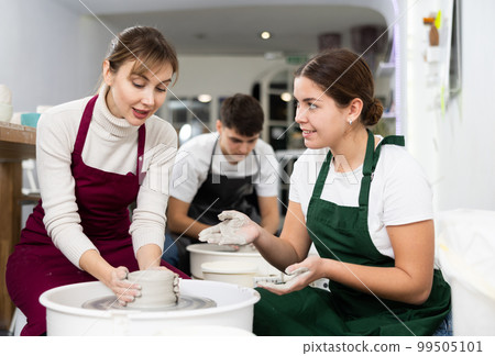 Two young women sculpt product on potter's wheel Two young women sculpt product on potter's wheel 99505101