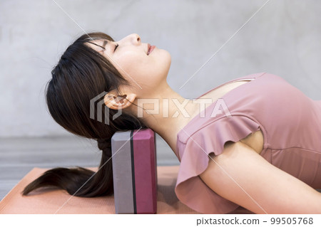 Young woman stretching neck using yoga block 99505768
