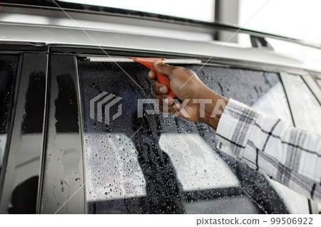 Cropped photo of a hand of black man with a sqeegee. Black man cleaning windows. Man wearing plaid shirt. 99506922