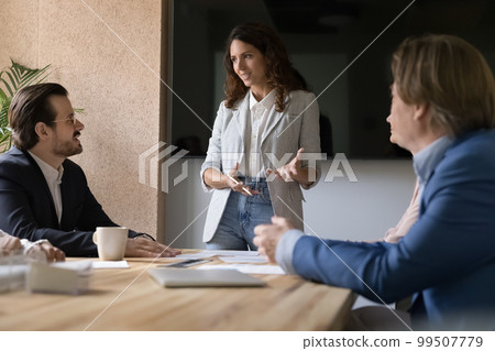 Positive confident business leader woman standing at conference table Positive confident business leader woman standing at conference table 99507779