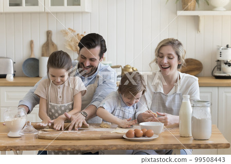 Couple of parents and kids in aprons teaching to bake, 99508443