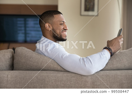 Cheerful excited handsome Black guy using mobile phone Cheerful excited handsome Black guy using mobile phone 99508447