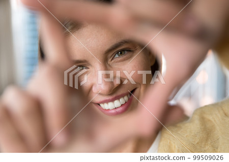 Happy young woman looking at camera through finger photo frame Happy young woman looking at camera through finger photo frame 99509026