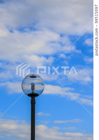 The blue sky and white clouds are reflected in the glass of the streetlight 99515097