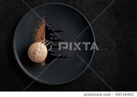Macaroon on a black plate garnished with chocolate sauce and cocoa powder. 99516462