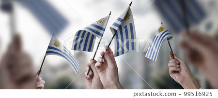 A group of people holding small flags of the Uruguay in their hands A group of people holding small flags of the Uruguay in their hands 99516925