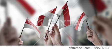 A group of people holding small flags of the Singapore in their hands A group of people holding small flags of the Singapore in their hands 99516927