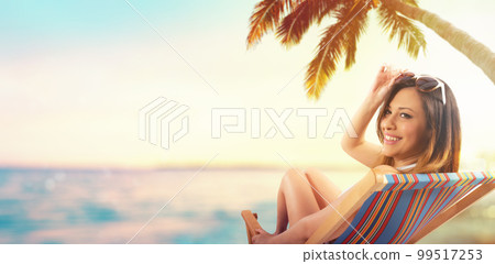 Beautiful girl sitting on a deck chair at the beach at sunset Beautiful girl sitting on a deck chair at the beach at sunset 99517253
