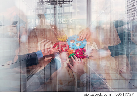 Business team connect pieces of colorful gears like a teamwork and partners on city buildings background Business team connect pieces of colorful gears like a teamwork and partners on city buildings background 99517757