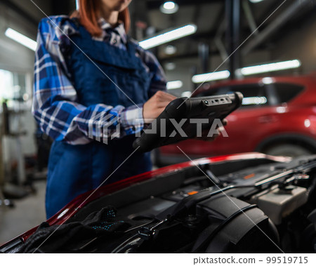Caucasian female auto mechanic uses a special computer to diagnose faults. Caucasian female auto mechanic uses a special computer to diagnose faults. 99519715