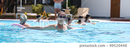 Young woman in sunglasses swims with aqua noodles in pool 99520448