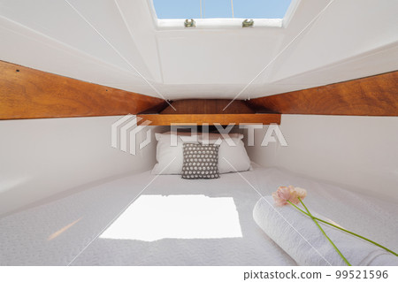 Bright luxury comfortable yacht inside with wood trim with white terry sheets, pillows, flower and sunbeams breaking through. Concept of luxury vacation on your own small yacht. 99521596