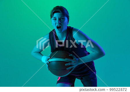 Sportive spirit and ambitions. Teen girl, basketball player posing with ball isolated over gradient green background in neon light. Concept of professional sport and hobby 99522872