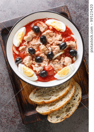 Ensalada Murciana is a traditional Spanish salad made with a combination of tomatoes, onions, tuna, hard-boiled eggs, and black olives closeup on the plate on the wooden board. Vertical top view 99523420