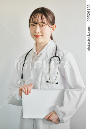 Young female doctor looking at camera standing with laptop Young female doctor looking at camera standing with laptop 99526103