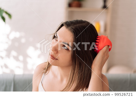 Woman enjoys doing herself a head massage with a scalp massager Woman enjoys doing herself a head massage with a scalp massager 99526721