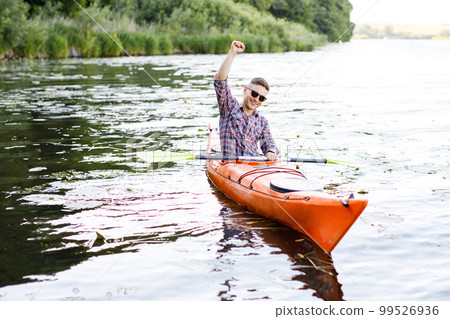 Adult caucasian man is sitting in a kayak and greetings. The concept of the water activities. 99526936