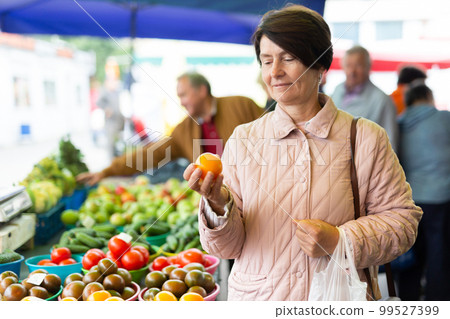 Aged woman customer buying vegetables in open-air market Aged woman customer buying vegetables in open-air market 99527399