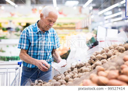 Elderly retired man buying potato in grocery department of supermarket 99527414