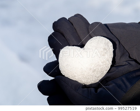 A heart made of snow is placed on the gloved hand. 99527519