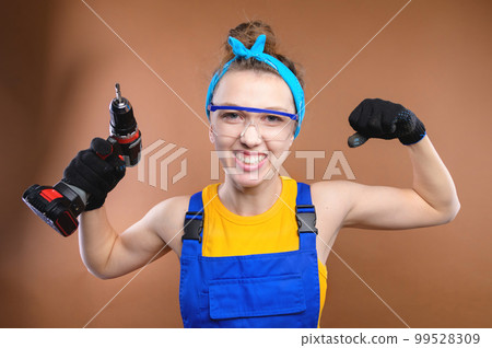 Smiling young caucasian woman in goggles with a screwdriver in her hands and in uniform stands in the studio Smiling young caucasian woman in goggles with a screwdriver in her hands and in uniform stands in the studio 99528309
