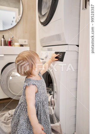 House cleaning. Happy baby girl one and a half, helper are having fun and smiling while in a bright apartment. Helps parents change bed linen and do laundry in the washing machine. 99528387