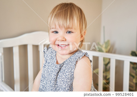 Happy baby girl one and half standing in the crib. Smiling 18 months child playing in sunny bedroom. Baby cot in the parent's bedroom Happy baby girl one and half standing in the crib. Smiling 18 months child playing in sunny bedroom. Baby cot in the parent's bedroom 99528401