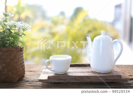 White tea cup and tall tea pot and Verbena plant in a basket pot wooden table balcony White tea cup and tall tea pot and Verbena plant in a basket pot wooden table balcony 99528534