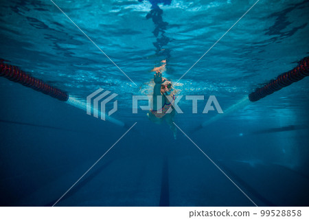 Fast and strong. Professional female swimmer in cap and goggles in motion, training in swimming pool indoor. Underwater view. Concept of sport, endurance, competition 99528858