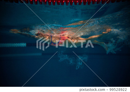 Bubbles. Professional female swimmer in cap and goggles in motion, training in swimming pool indoor. Underwater view. Concept of sport, endurance, competition Bubbles. Professional female swimmer in cap and goggles in motion, training in swimming pool indoor. Underwater view. Concept of sport, endurance, competition 99528922