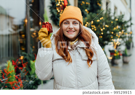 Woman holding a one Christmas gift outdoor in winter time. Snowfall. Fir-tree, garland backround. Concept of shopping, holidays and happiness Christmas. Woman holding a one Christmas gift outdoor in winter time. Snowfall. Fir-tree, garland backround. Concept of shopping, holidays and happiness Christmas. 99529915