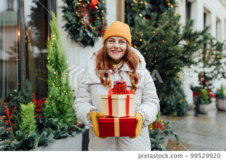 Happy young beautiful excited woman holding gift boxes in hands and smile on winter street. Winter holidays sale. Concept of shopping, holidays and happiness christmas. Happy young beautiful excited woman holding gift boxes in hands and smile on winter street. Winter holidays sale. Concept of shopping, holidays and happiness christmas. 99529920