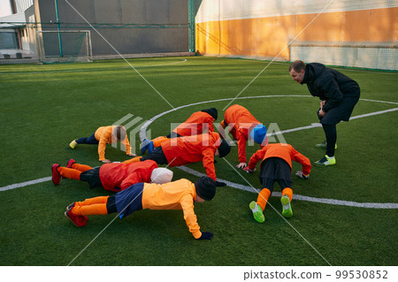 Little boys, children, football players training with professional coach outdoors on sport field. Doing push ups. Concept of sport, childhood, active lifestyle 99530852