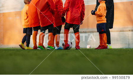 Cropped image of male legs on grass of sports field outdoors. Children playing football with coach. Concept of sport, childhood, active lifestyle 99530879
