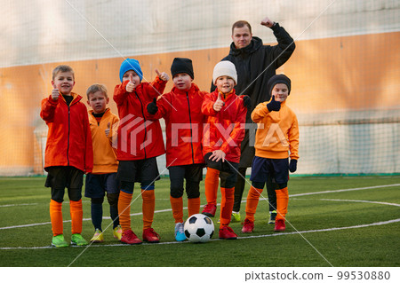 Group of boys, children, football players in uniform standing in a line on sports field grass outdoor, posing with coach. Concept of sport, childhood, active lifestyle 99530880